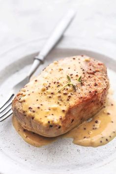 a piece of meat covered in gravy on a white plate with a fork