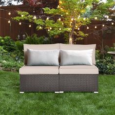 an outdoor couch with two pillows on it in the grass next to a table and tree