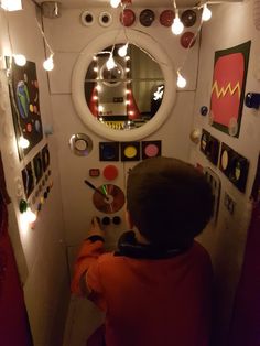 a boy is sitting in front of a mirror and looking at his artwork on the wall