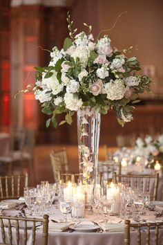 a tall vase filled with white and pink flowers sitting on top of a dining table