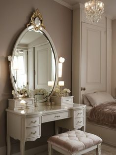 a white dressing table with a mirror and stool next to it in front of a bed