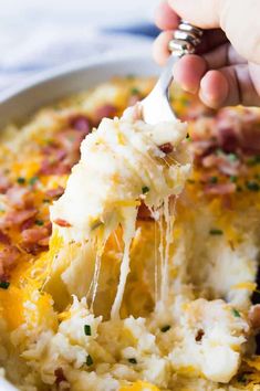 a person holding a spoon full of mashed potato casserole with bacon and cheese