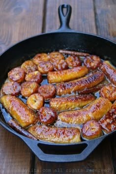 sausages and bananas cooking in a cast iron skillet on a wooden table top