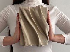 a woman is covering her face with a piece of cloth in front of her head