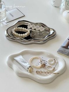 two white trays with pearls and bracelets on top of a table next to a book