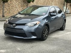 a gray toyota car parked in front of a stone wall with trees on the side