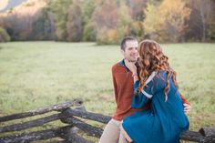 a man and woman standing next to each other near a fence in front of a field