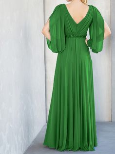 a woman in a long green dress standing against a wall with her back to the camera