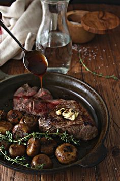 the steak is being drizzled with sauce on top of potatoes and mushrooms