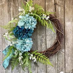 a wreath with blue flowers and greenery hanging on a wooden wall