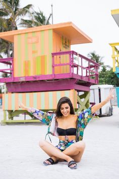 a woman sitting on the ground in front of colorful beach huts with her arms outstretched