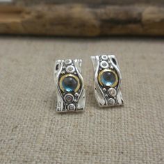 "Stunning Sterling Silver Rocks N' Rivers Stud Earrings with 10K Bezel Center London Blue Topaz with 10K bezel CZ accents Earring: 1/2\" long and 1/4\" wide.  Post back.  Signature on back. Textured finish. Signed by the Artist Nicely boxed with silver cloth. Ships in 3 to 5 days. Ships Free within the USA 21 Day Returns Items must be returned in new unworn condition." Sterling Silver Earrings With Accent Stones, Topaz Anniversary Earrings With Gemstone Accents, Blue Bezel Set Earrings For Gift, Sterling Silver Bezel-set May Birthstone Ring, Silver Topaz Earrings With Gemstone Accents, Gift Amethyst Bezel-set Jewelry, Formal Bezel-set Cubic Zirconia Earrings, Adjustable Bezel-set Cubic Zirconia Jewelry, Thistle Design