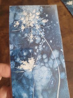 a hand holding up a piece of paper with flowers on it and snow flakes in the background