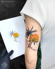 a person with a tattoo on their arm holding up a piece of paper that has an image of two palm trees