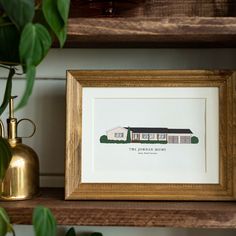 a framed print of a house sits on a shelf next to a potted plant