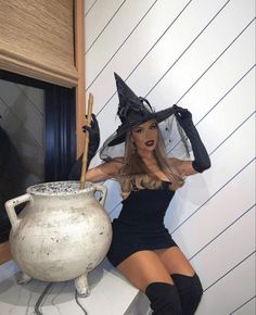 a woman in a witch costume sitting on a counter next to a pot and broom