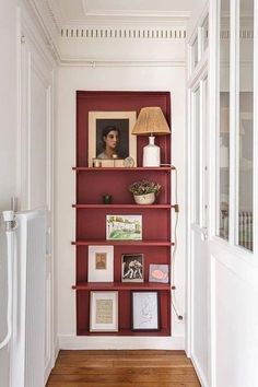 a red book shelf with pictures on it and a lamp in the corner next to it