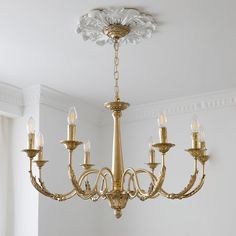 a gold chandelier hanging from the ceiling in a room with white walls and windows