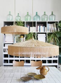 a dining room table with two hanging lamps above it and bookshelves in the background