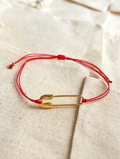 a red string bracelet with an arrow charm on the end and a gold plated bar