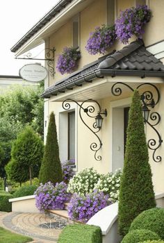 a house that has some flowers in the windows and bushes on the side of it