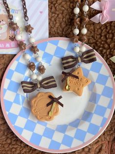 two decorated cookies are on a plate next to a card and chain necklaces with bows