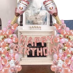 a happy birthday balloon arch with champagne bottles and pink, gold and white balloons in front of a fireplace