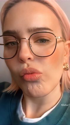 a woman with pink hair wearing glasses and looking at the camera while she has her face close to the camera