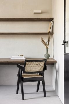 a chair sitting in front of a table with a vase on top of it next to a book shelf