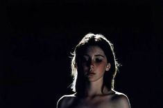 a woman is standing in the dark with no shirt on and her eyes are half closed