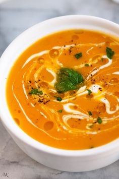 a white bowl filled with carrot soup on top of a table next to a spoon