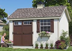 a white shed with brown shutters and flowers in the window boxes on the side