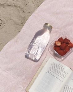 an open book and some strawberries in a plastic container next to a water bottle