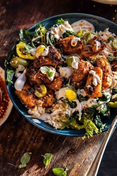 a blue plate topped with chicken, rice and veggies next to a bowl of sauce