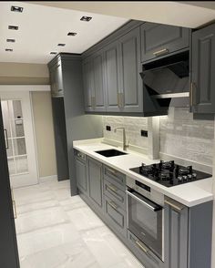 a kitchen with gray cabinets and white counter tops, an oven and sink are shown