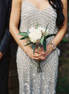 a woman in a silver dress holding a white rose and green leafy boutonniere