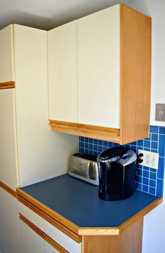 a coffee maker sits on top of a counter in a kitchen with white cabinets and blue tile