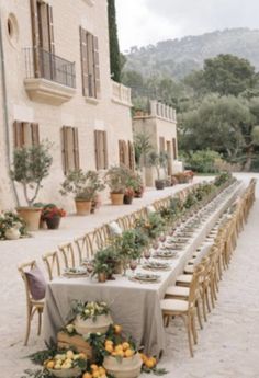 a long table is set up outside in front of a building with potted plants