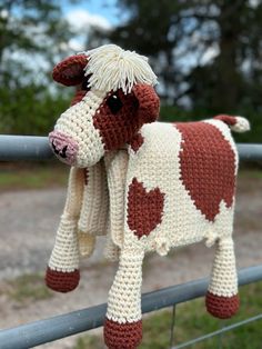 a crocheted cow hanging on a fence with hearts in it's ear