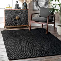 a living room area with a chair, rug and sideboard in black color on wooden flooring