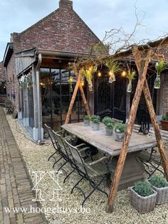 an outdoor dining area with tables and chairs in front of a brick building that has potted plants on it