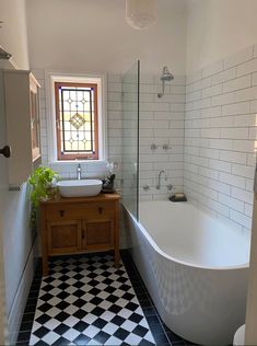 a white bath tub sitting next to a sink in a bathroom with black and white tiles