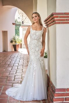 a woman in a white wedding dress leaning against a brick wall and posing for the camera