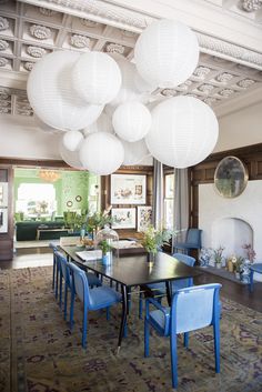 a dining room table with blue chairs and white lanterns hanging from the ceiling above it