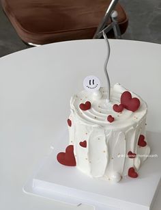 a white cake with red hearts on it sitting on top of a table next to a pair of scissors