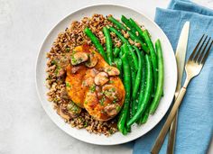 a white plate topped with green beans and chicken covered in mushrooms next to silverware