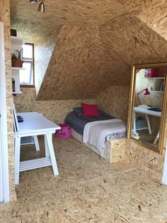 a bedroom with a bed, desk and mirror on the wall in an unfinished room