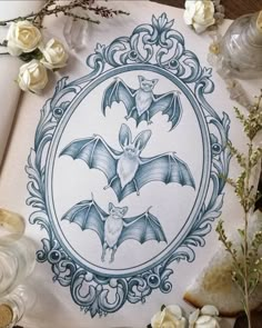 a drawing of a bat in a frame surrounded by flowers and other items on a table