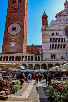 people are walking around in front of an old building with a clock on the side