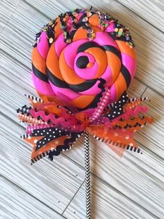 an orange and pink lollipop on a stick with black polka dots, sprinkles and ribbons